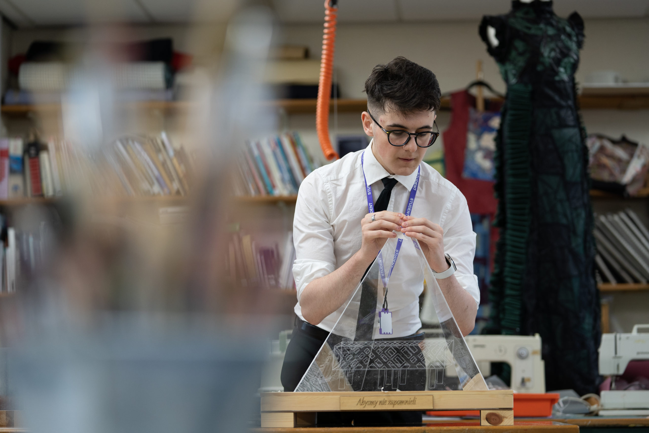A student can be seen in a Technology class working with materials to create a wood and glass sculpture.