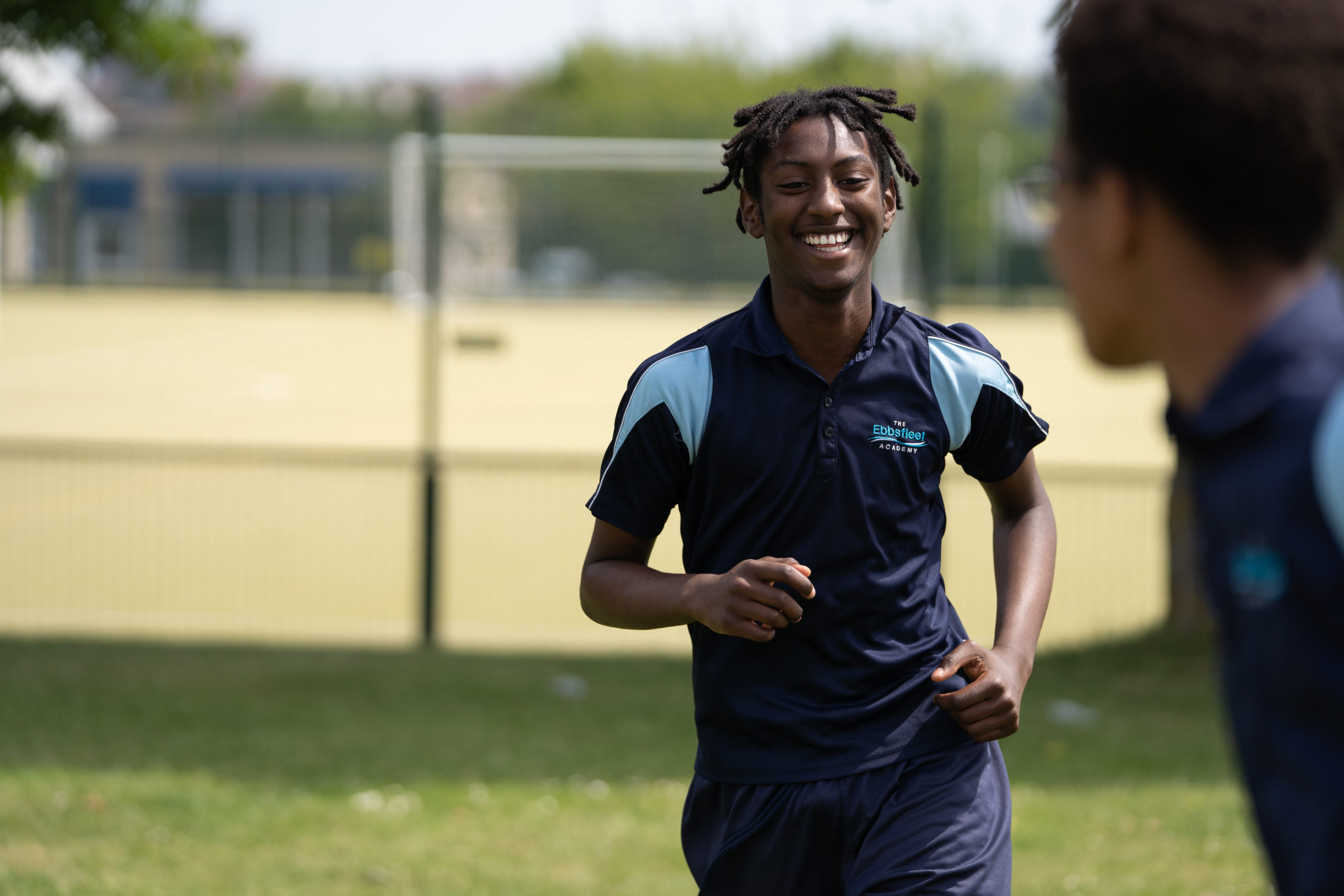 A male student is seen running on the school grounds, wearing his PE Kit and a smile on his face.