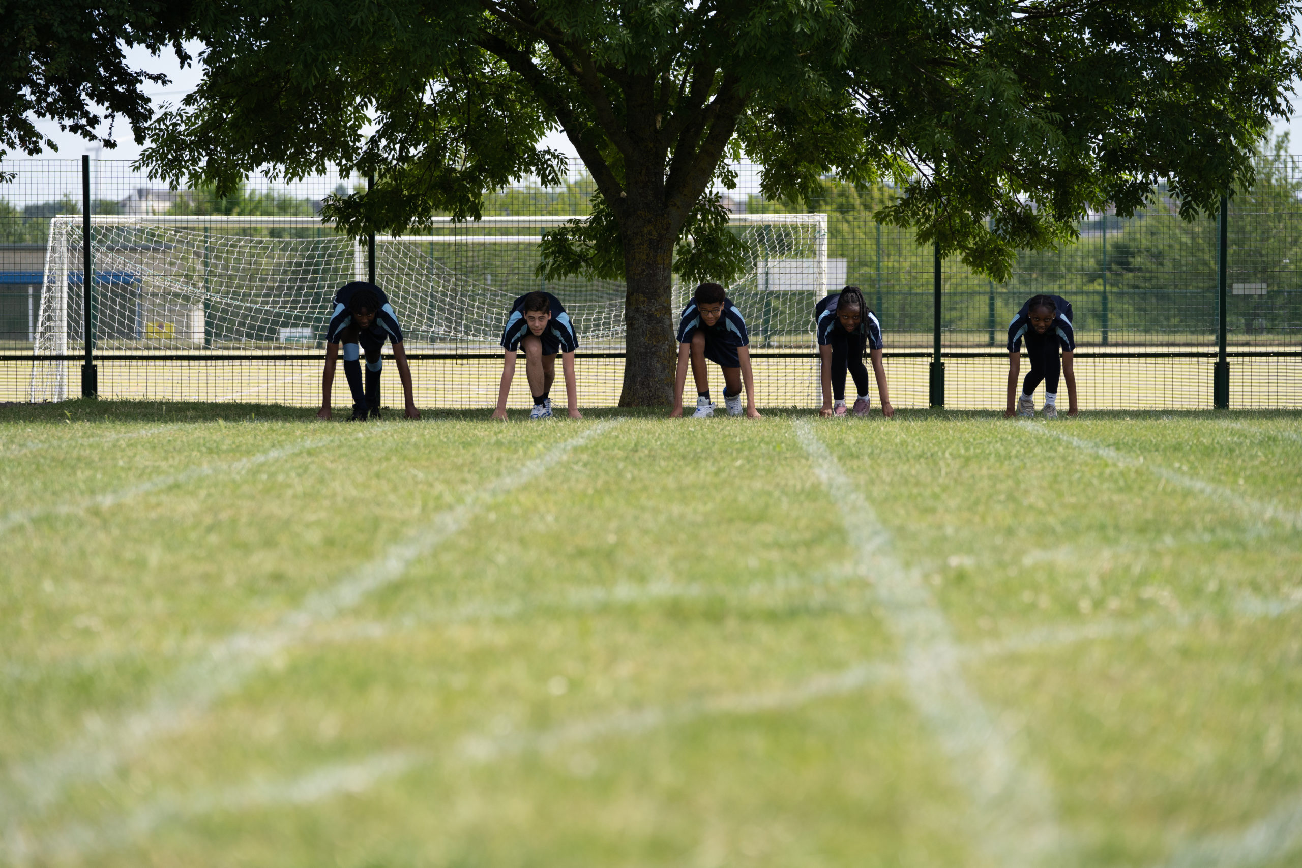 Five students are seen dressed in their PE Kit, poised in a kneeling position, ready to run in a race.