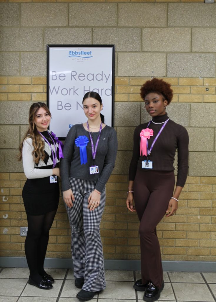 Three female students pose for the camera wearing rosettes from the Head Student Elections at Ebbsfleet Academy.