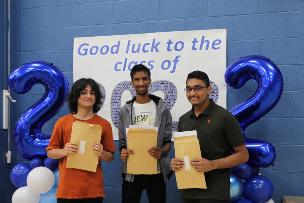 Three male Ebbsfleet Academy students are pictured holding their results envelopes and smiling for the camera on GCSE Results Day 2022.