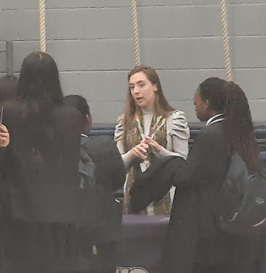 Photo showing a small group of academy students listening to a speaker behind a stall at an event in the Sports Hall.