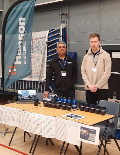 Two male representatives from the company Hanson are pictured standing behind a stall at a Careers Event in the academy's Sports Hall.