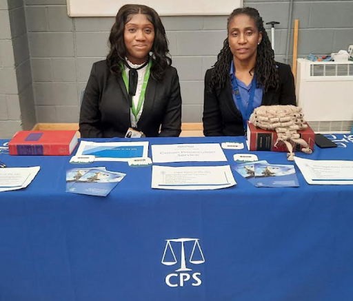 Two female representatives from the Crown Prosecution Service are pictured sitting behind a stall at a Careers Event in the academy's Sports Hall.