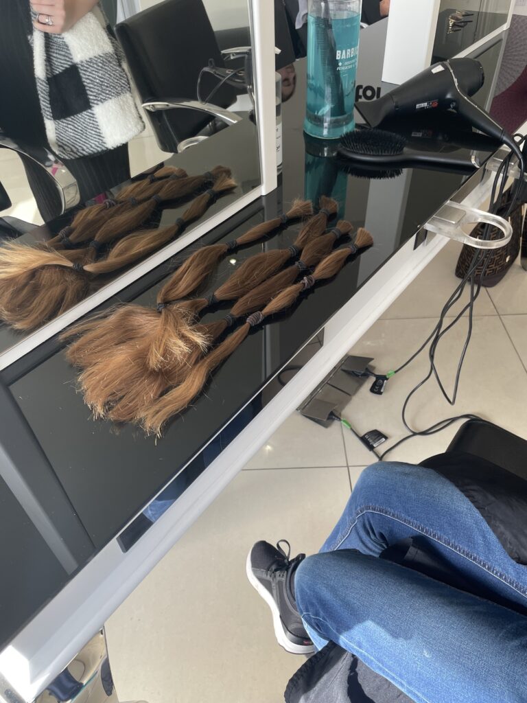 Four long ponytails are seen chopped off from a female student's hair and laid out onto a worktop in a hairdresser's salon.