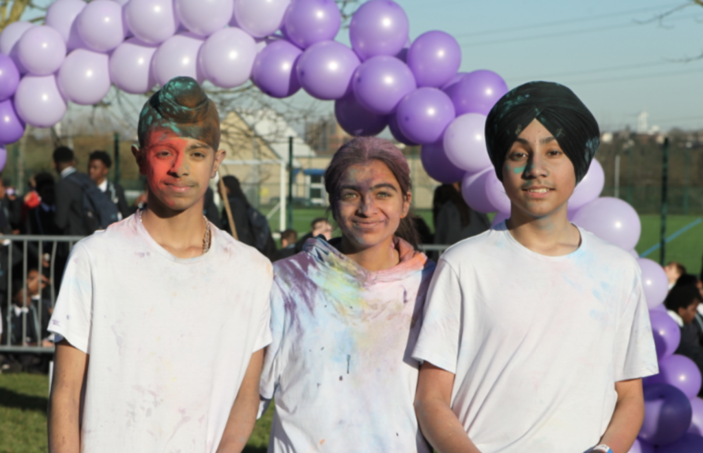 Three students are pictured smiling for the camera with coloured powder on their clothes after celebrating the Hindu festival Holi on the academy grounds.