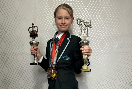 An Ebbsfleet Academy student is pictured kneeling on the floor posing with the Karate medals and awards she has won.