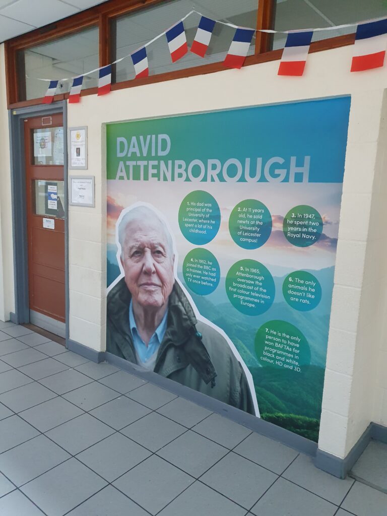 Photo showing a corridor in the Ebbsfleet Academy building with a wall featuring the image of and information about Sir David Attenborough.