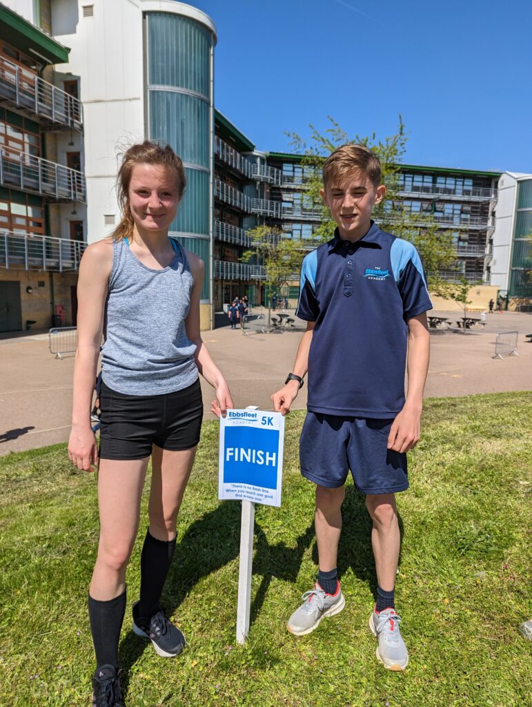Two students stood either side of the finish line sign on the academy grounds on a sunny day.