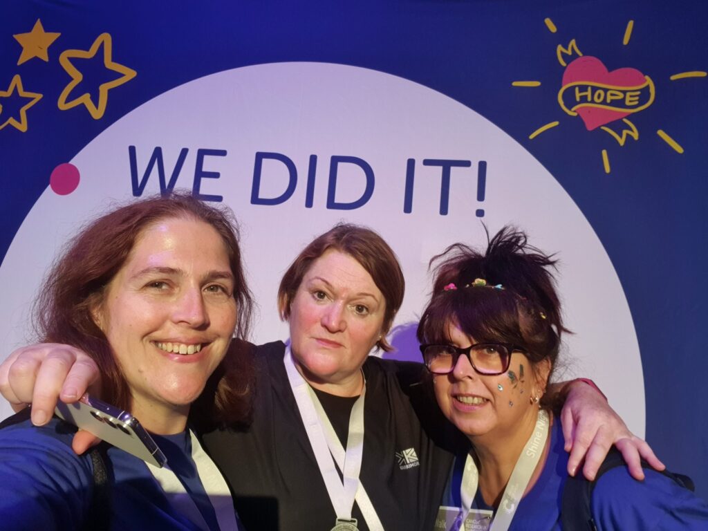 three staff members posing at a 'we did it' sign after completing a walking marathon