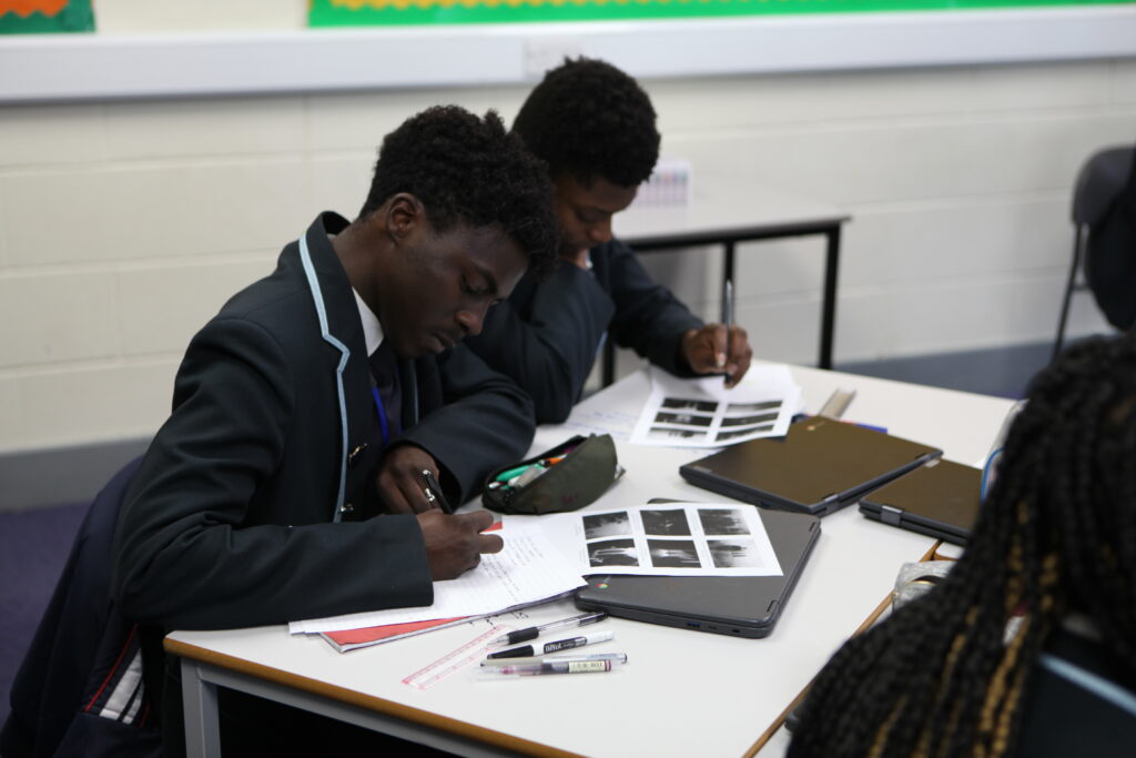 Three Year 11 Ebbsfleet Academy students are seen concentrating on their work, whilst sat at their desks during a Macbeth Workshop.