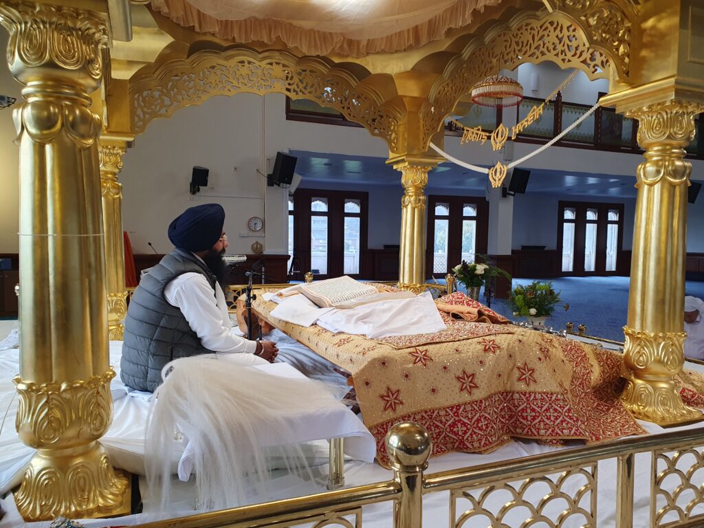 A Gurdwara leader reading text on an altar at the front of a large room in the building.