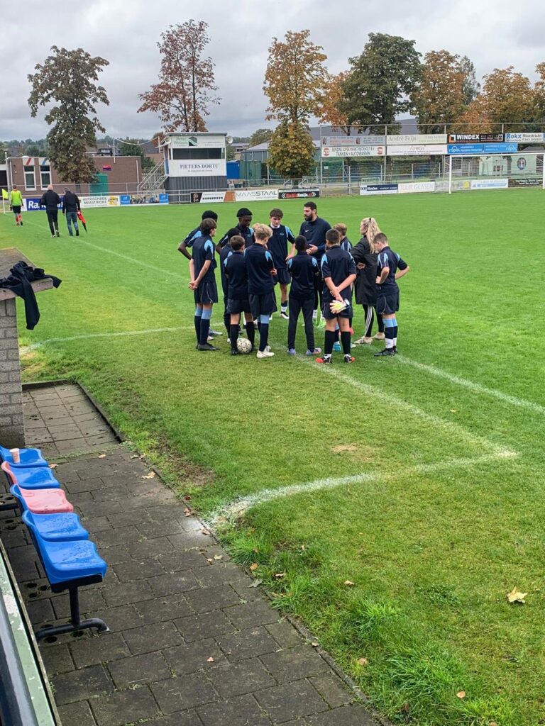 Students stood in a huddle with 2 adults on a football pitch