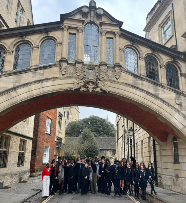 A large group of Year 11 and 12 students are pictured stood together for the camera under an ornate bridge on the grounds of Oxford University.