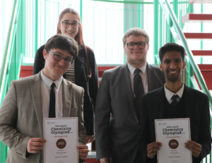 Four students stood on a staircase showing off their certificates for the Chemistry Olympiad