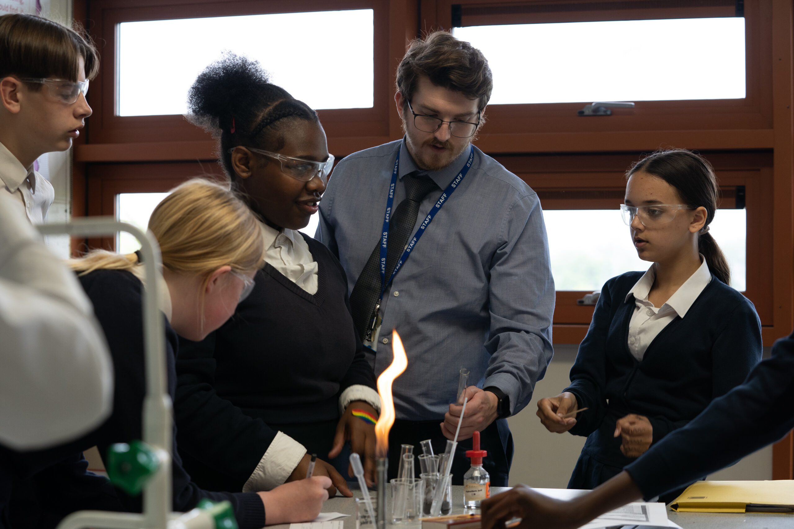 A teacher and several students looking at a bunsen burner