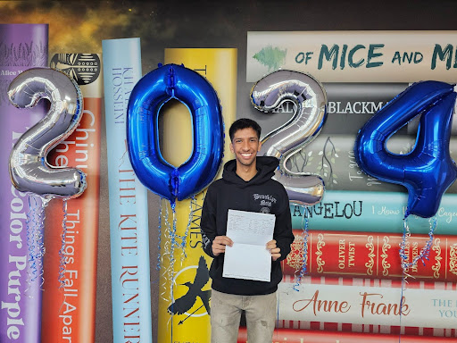 A male Post-16 student is seen smiling for the camera, whilst holding up his A-Level results.