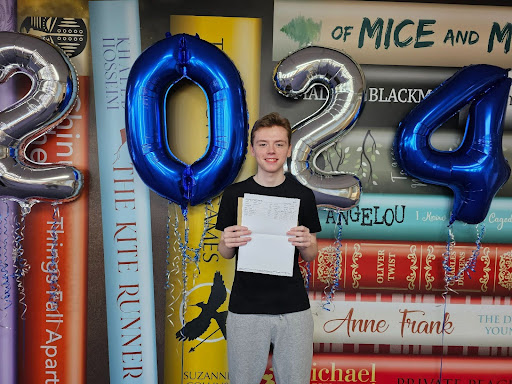 A male Post-16 student is seen smiling for the camera, whilst holding up his A-Level results.