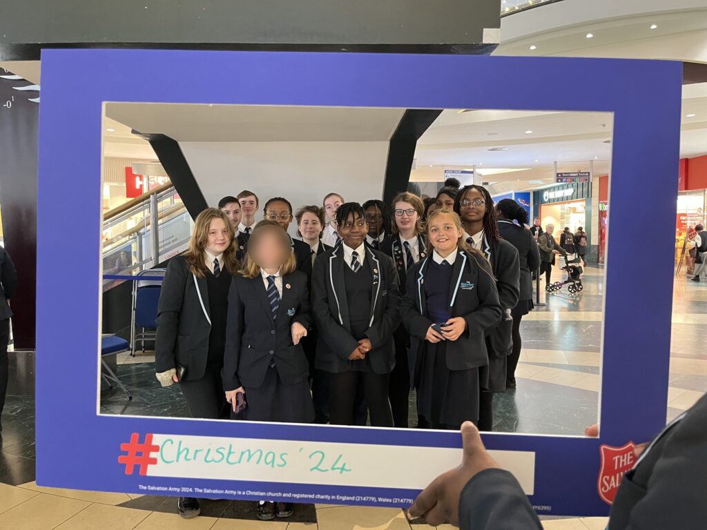 A group of students smiling for a photo behind a frame being held up which reads "Christmas '24"
